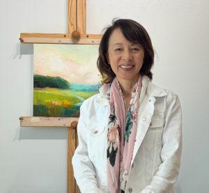 Naomi Bautista in her studio beside one of her landscape paintings